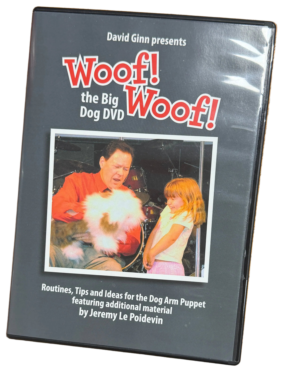 DVD case titled 'Woof! The Big Dog DVD' on a wooden surface with a person wearing a purple shirt in the background.