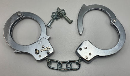 Metallic handcuffs with a key on a gray background