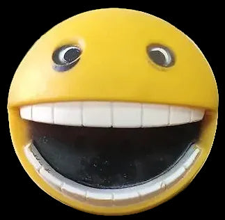 Yellow emoji-shaped object with a wide smile on a surface with plants in the background