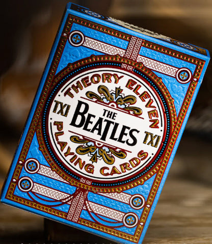 Playing card deck with The Beatles 'Theory Eleven' branding on a wooden surface.