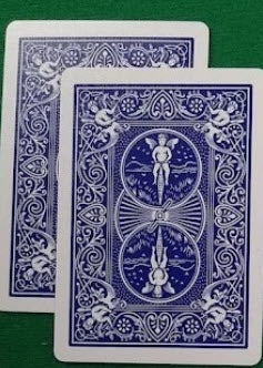 Two blue playing cards with a central design on a green surface