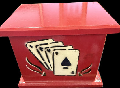Red wooden box with cut-out design of playing cards on a wooden surface.