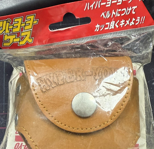 Brown leather pouch with a button in clear packaging on a red background with Japanese text.