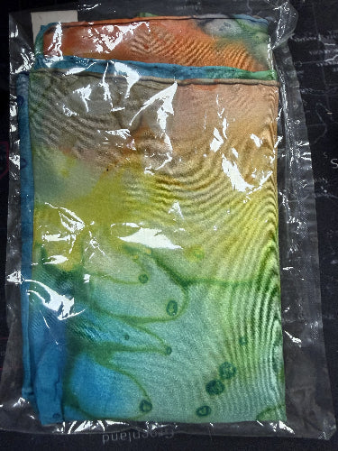 Colorful fabric with a tie-dye pattern in blue, green, and orange on a clear plastic bag.