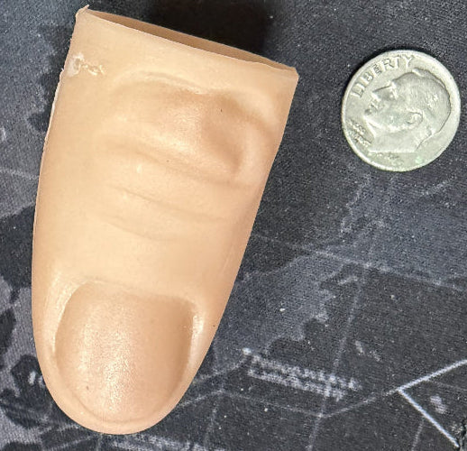 Prosthetic finger next to a coin on a textured surface