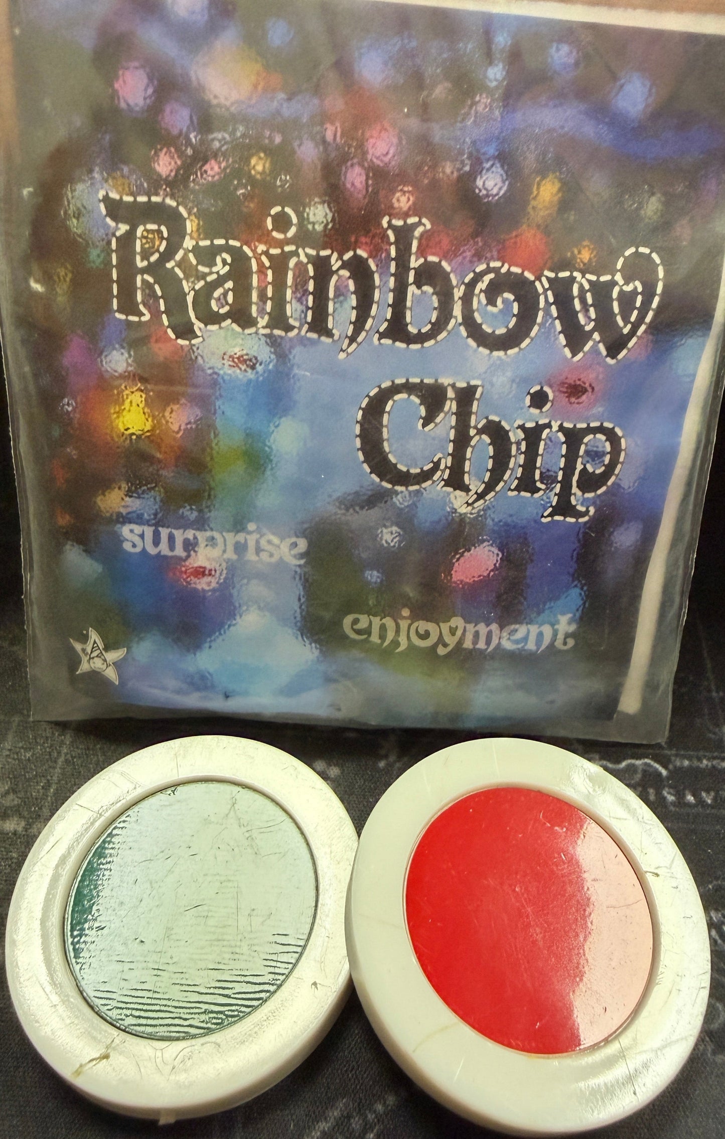 Packaging of Rainbow Chip with two round colorful items on a dark surface