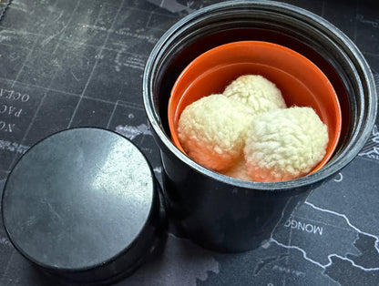 Metal container with orange lid holding white spherical objects on a map background