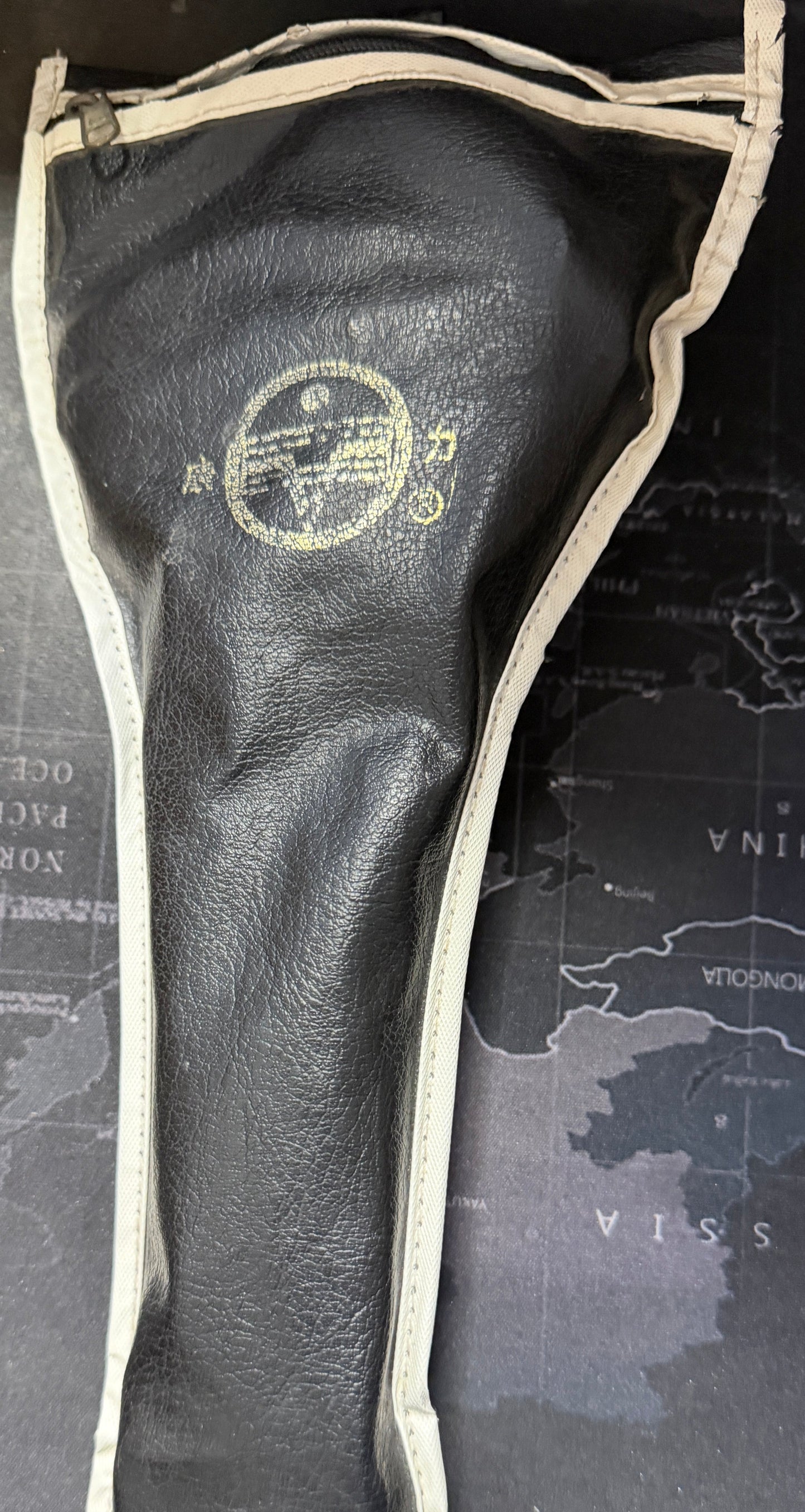 Black golf club head cover with a logo on a map-themed surface