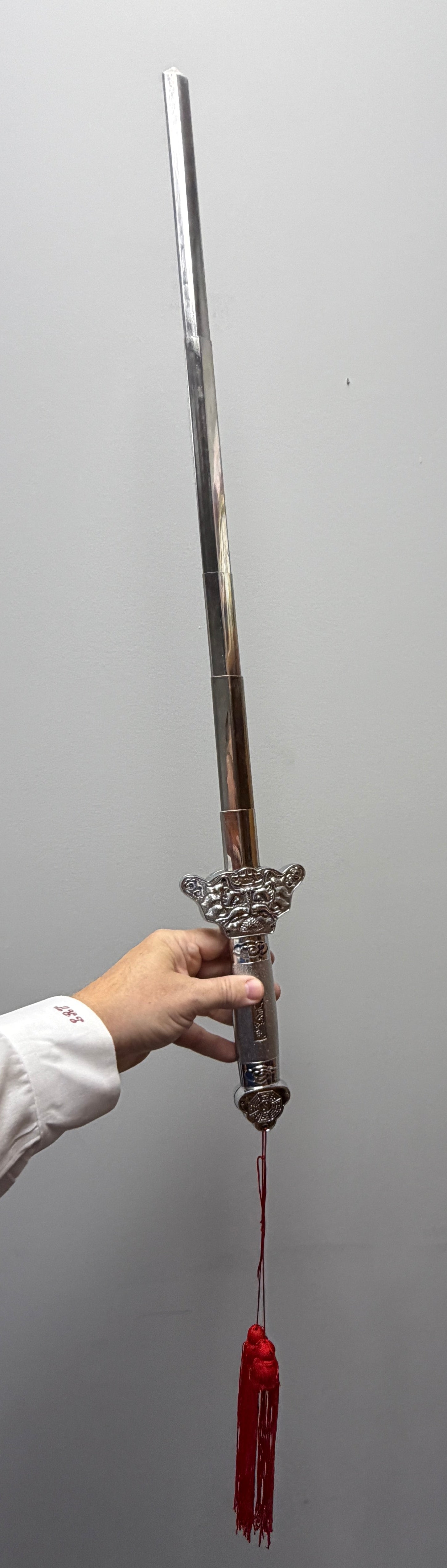 Person holding a sword with a red blade against a plain wall