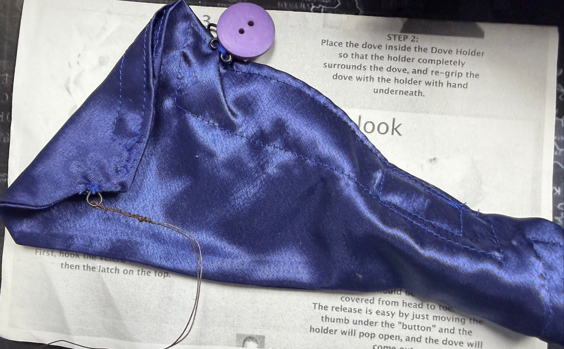 Purple satin bag with a button on top of a printed manual