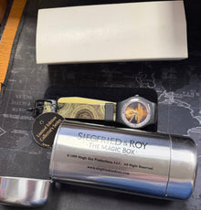 Silver cylindrical container with 'Siegfried & Roy' branding on a textured surface.