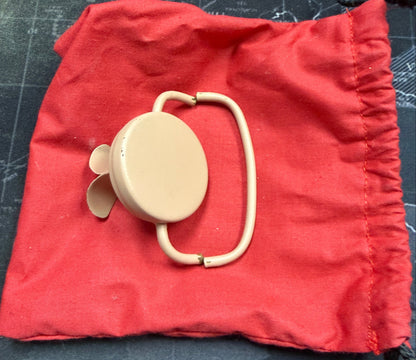 Beige circular object with a handle on a red drawstring bag against a dark background