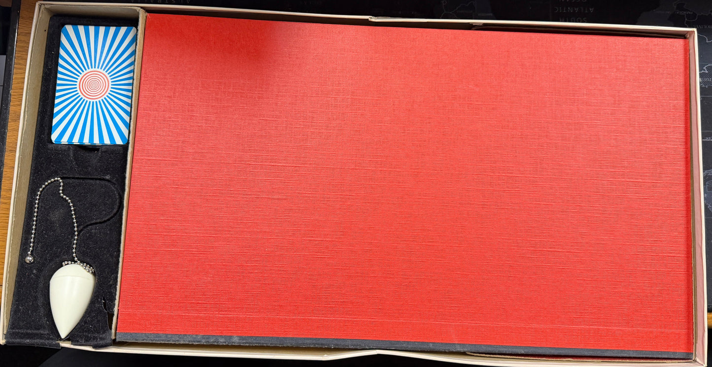 Open box containing a red item, blue and white card, and a small object on a wooden surface.