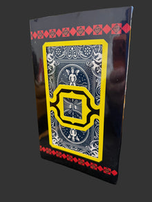 Playing card with decorative design on a black border, held by a hand.