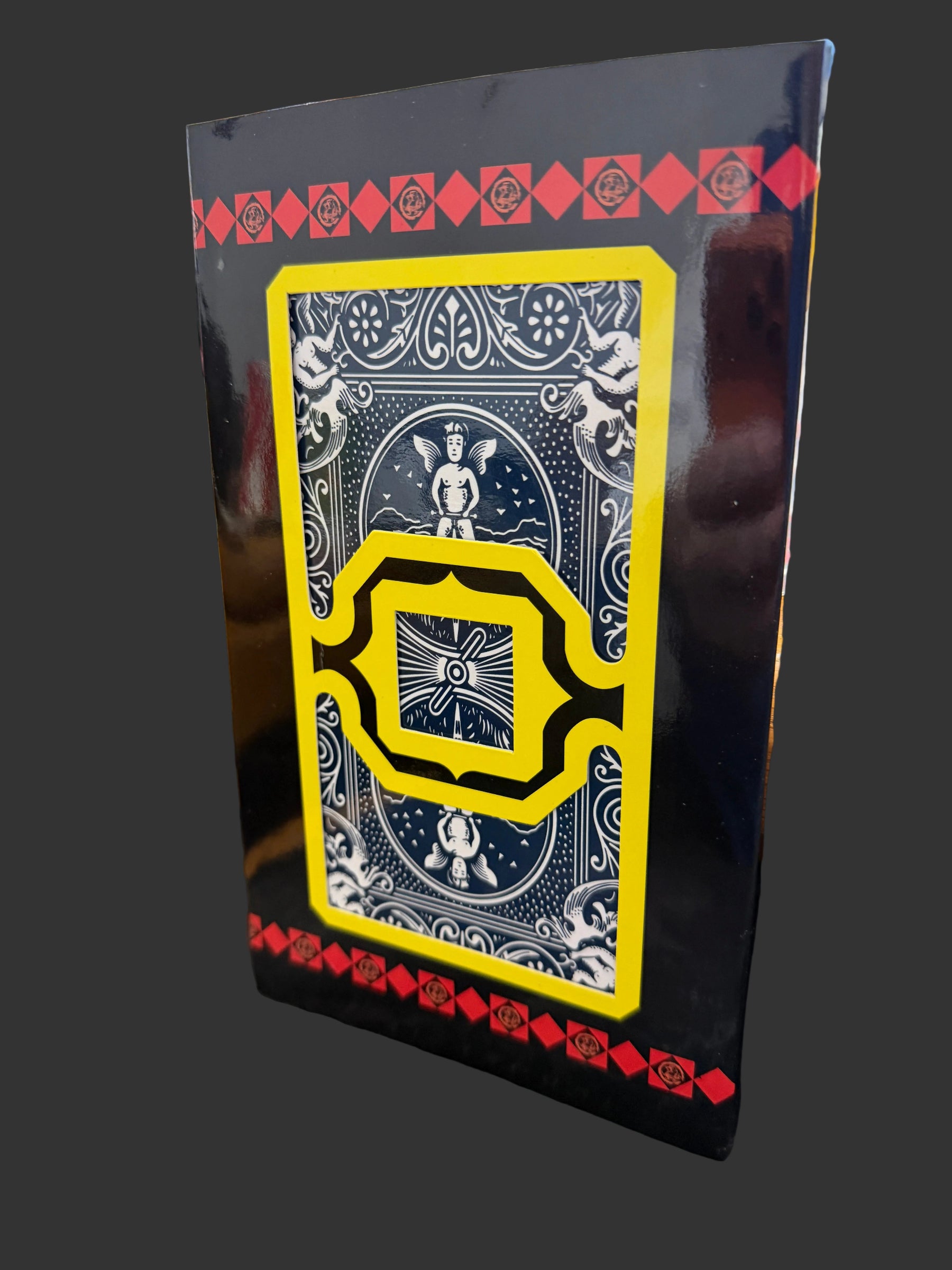 Playing card with decorative design on a black border, held by a hand.