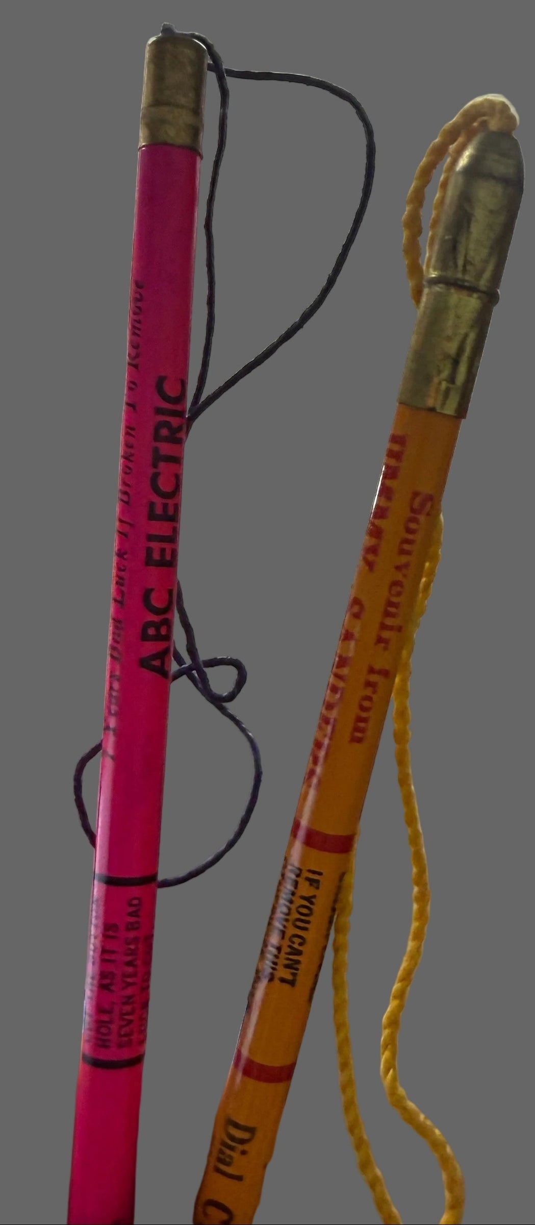 Pink pencil with decorative top held by a hand, against a background of shelves with various items.