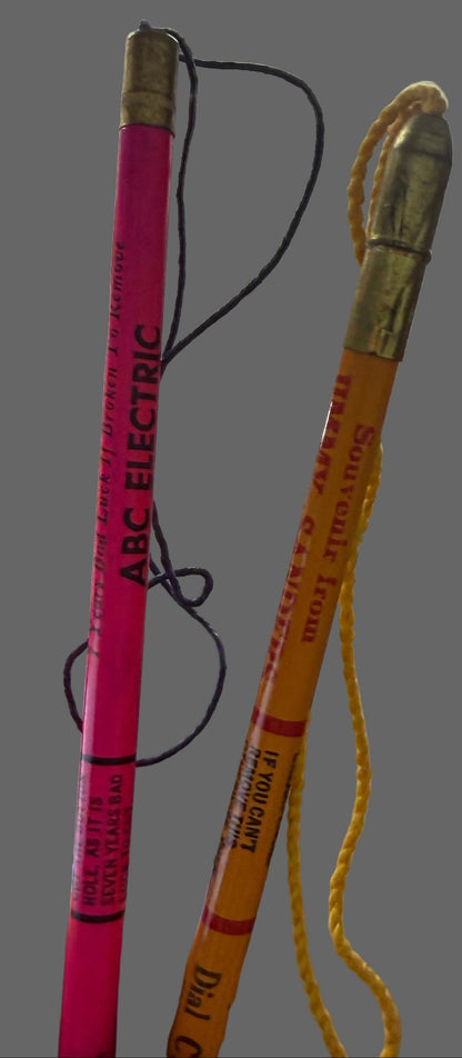 Pink pencil with decorative top held by a hand, against a background of shelves with various items.