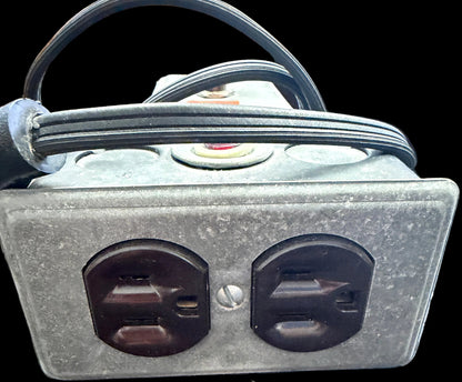 Metallic electrical outlet with two sockets on a textured surface.