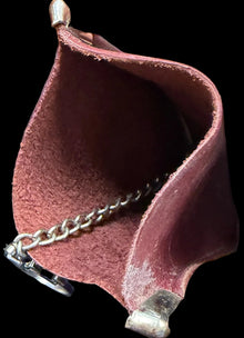 Close-up of a hand holding a small pink leather pouch with a chain, against a dark surface with text.