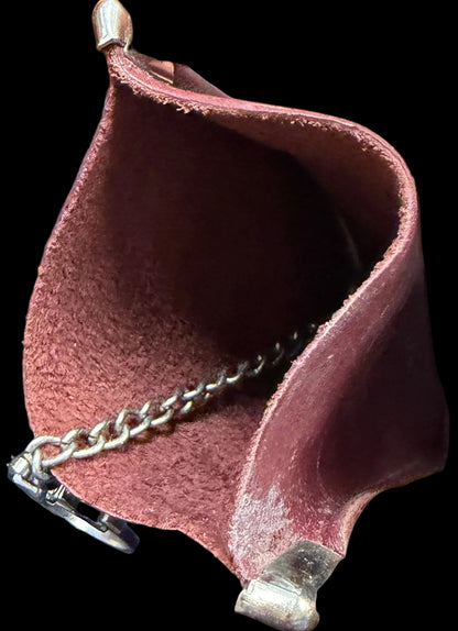 Close-up of a hand holding a small pink leather pouch with a chain, against a dark surface with text.