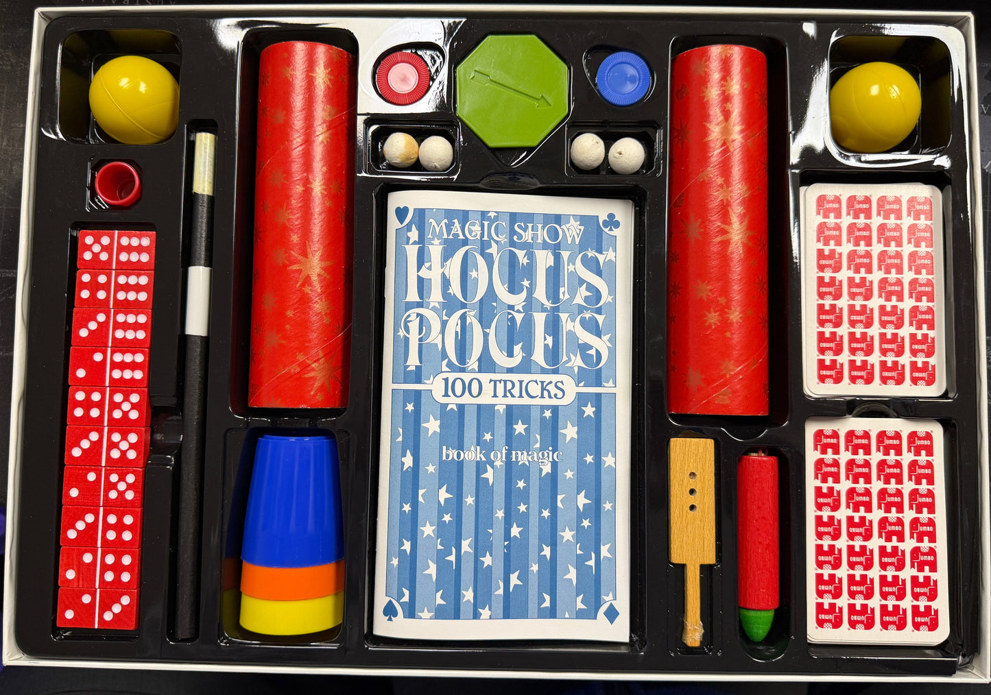 Magic show kit with cards, dominoes, and other props on a dark surface