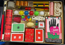 Magic trick set with various props and cards in a box on a table.