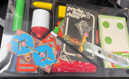 Close-up of a magic show kit with cards, darts, and other props in a clear plastic case.