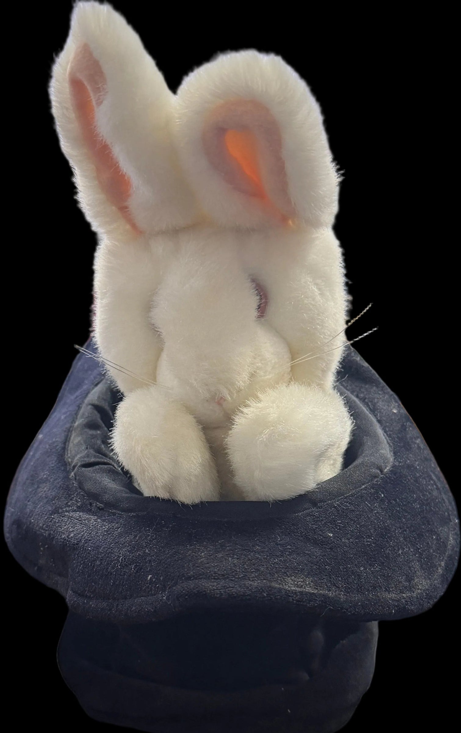 Plush toy rabbit in a dark hat on a desk with computer equipment in the background