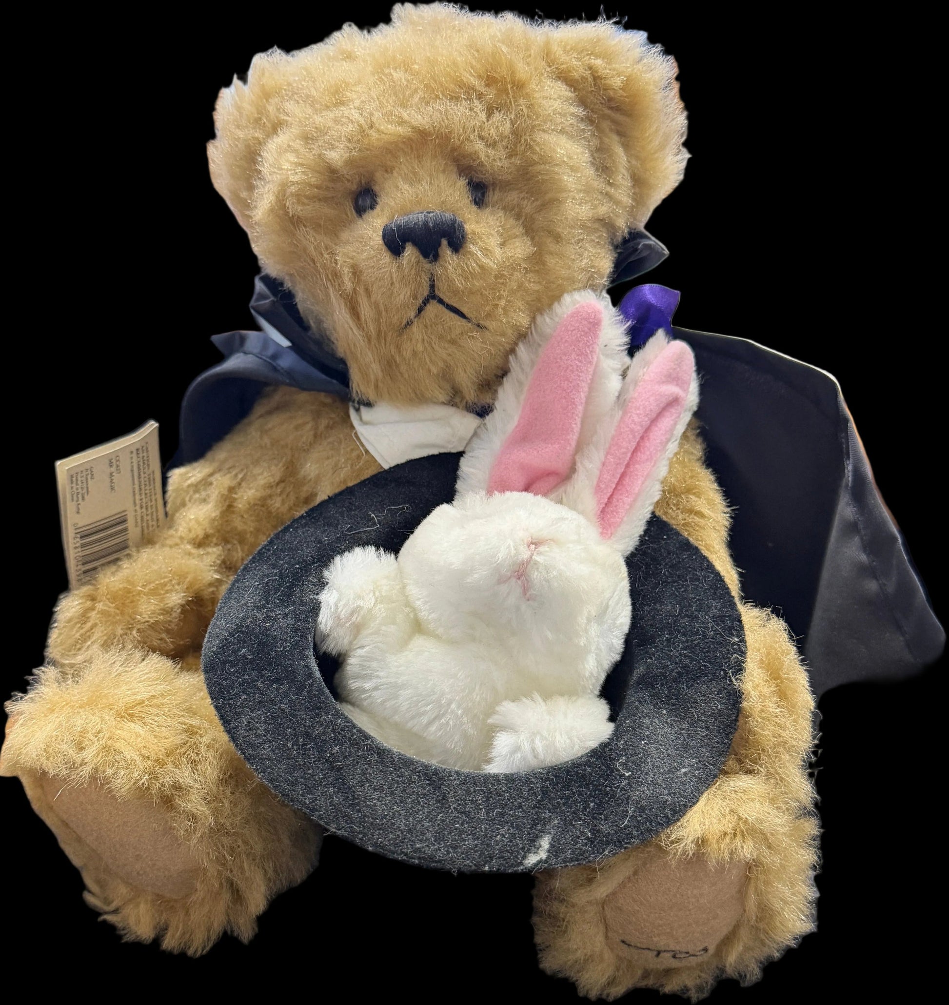 Teddy bear with bunny ears and black hat in a store display case.
