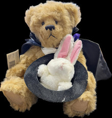 Teddy bear with bunny ears and black hat in a store display case.