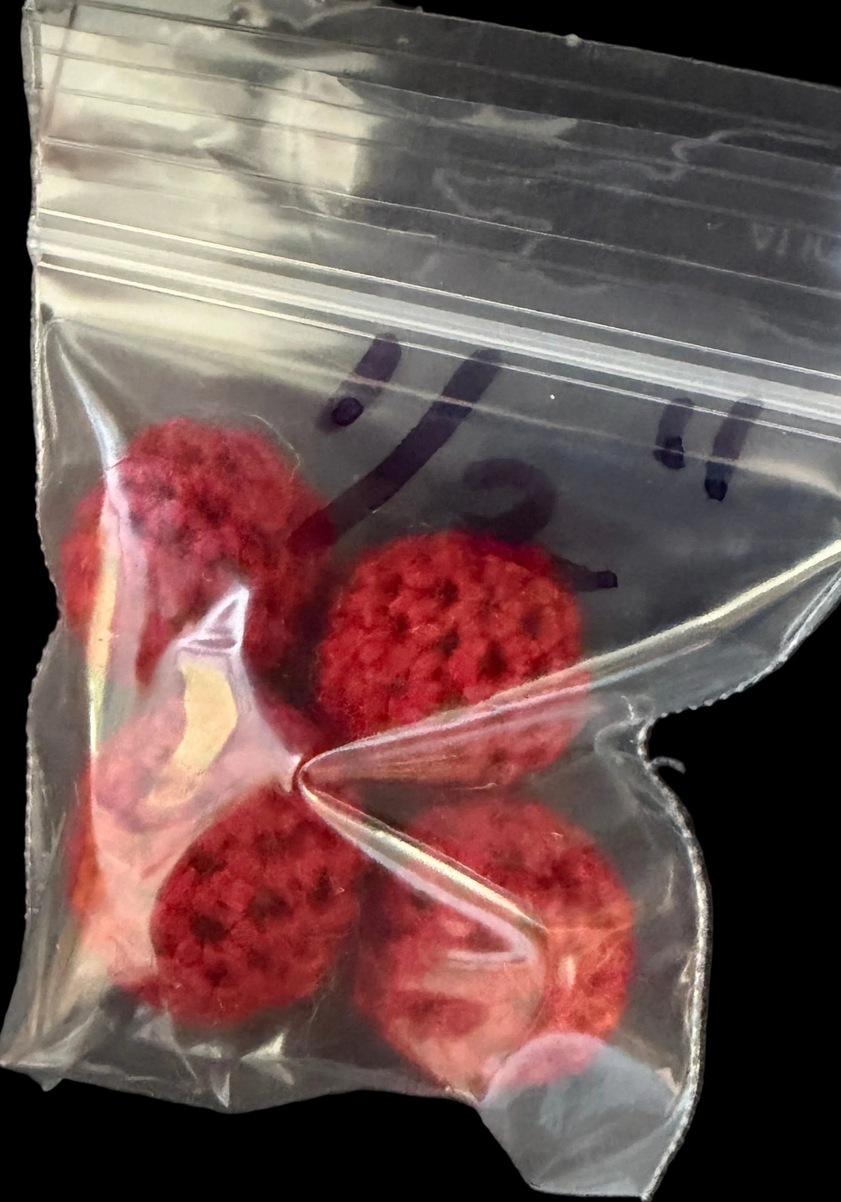 Red textured objects in a clear plastic bag on a dark surface