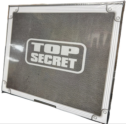 Top Secret box with a textured surface and metallic border, surrounded by other items.