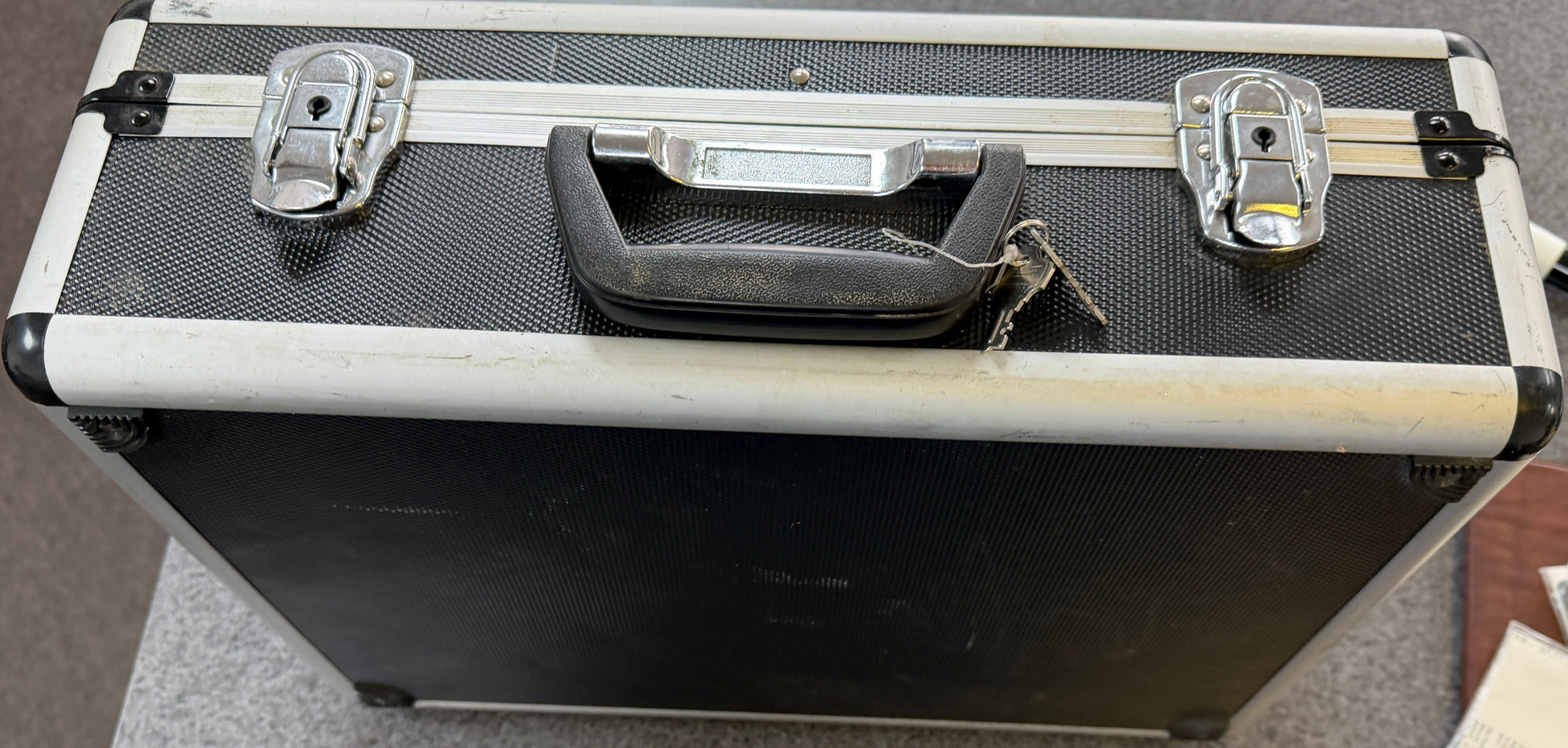 Black and silver briefcase on a gray surface with a brown leather item and money in the background.