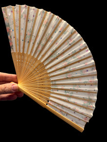 Handheld fan with floral pattern held by a person indoors.