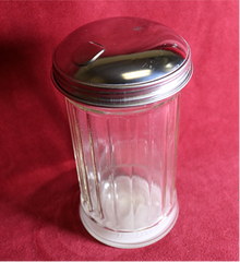 Glass container with silver lid on a red background, featuring MJM Magic branding.