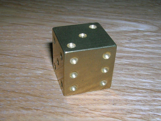 Gold die with six dots on a wooden surface