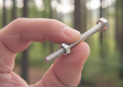 Hand holding a metal screw against a blurred background