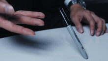 Close-up of hands holding a pen on a white surface with a dark background