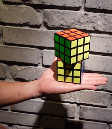 Hand holding a partially solved Rubik's Cube in front of a brick wall.