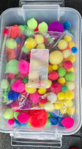 Colorful pom-poms in a clear container on a black surface