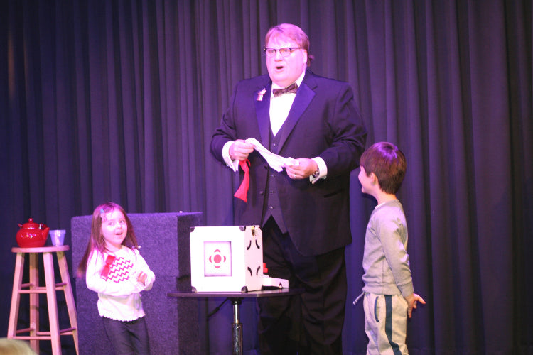 Man in a suit performing magic tricks on stage with two children