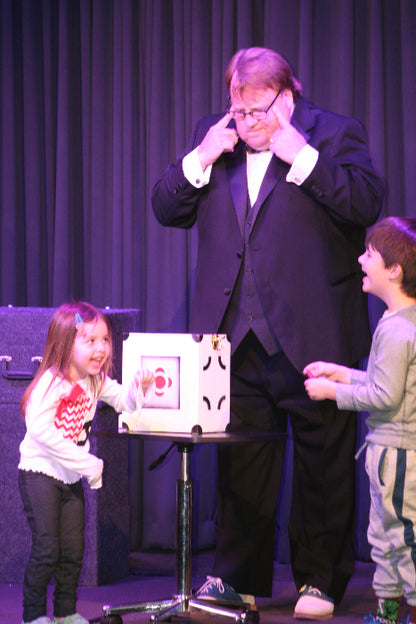 Two people lying on a stage with a box between them, one person is wearing a suit and tie.