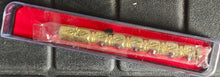 Gold-colored tool or device in a clear plastic case on a textured gray surface