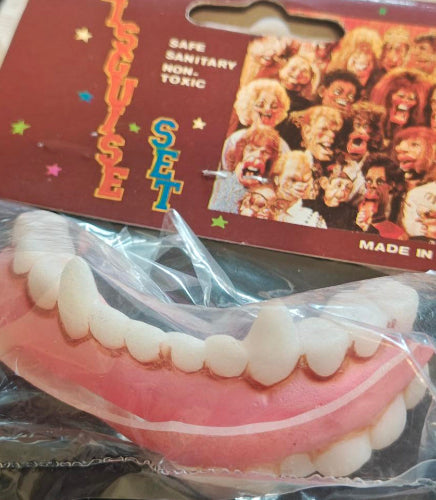 Packaged novelty teeth with a colorful label on a dark background
