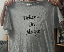 Gray t-shirt with 'Believe In Magic' text held by a person.