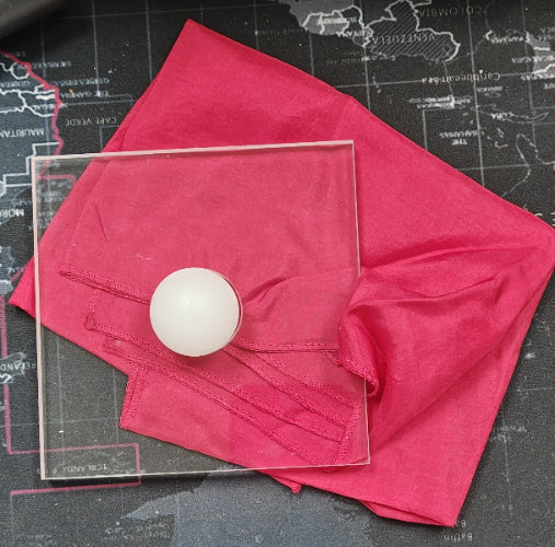 White ball on a transparent square on a pink cloth with a black background