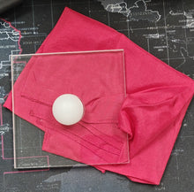 White ball on a transparent square on a pink cloth with a black background
