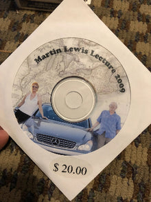 Disc with 'Martin Lewis Lecture 2009' text and images of two people with a car, held over a carpeted floor.