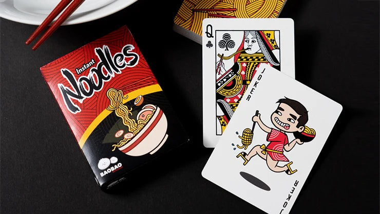 Noodle package and playing cards on a black surface