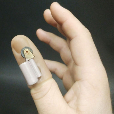 Hand holding a small electronic device on a finger against a dark background